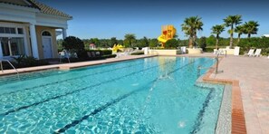 A swimming pool with clear blue water, a diving board, and lounge chairs.