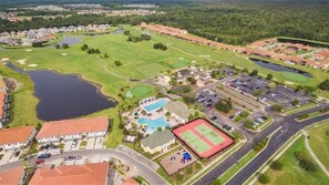 Vue aérienne d’un quartier résidentiel avec des maisons, un terrain de golf, une piscine, des courts de tennis et un parking.