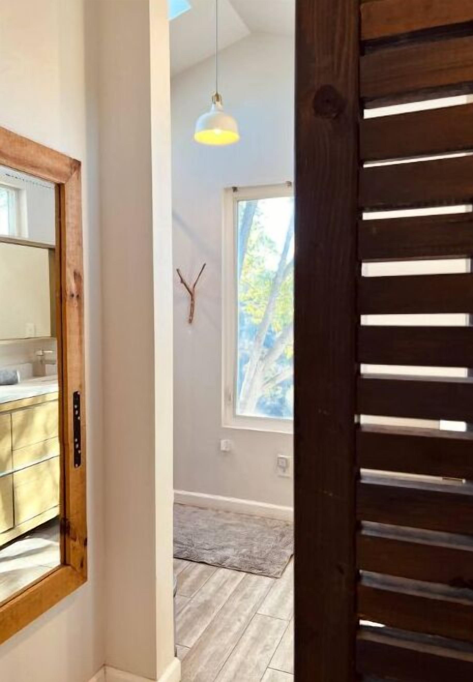 A hallway with a wooden door, a window with a view of trees, and a pendant light.