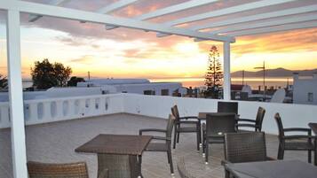 A rooftop terrace with wicker furniture and a view of the sunset over the city.