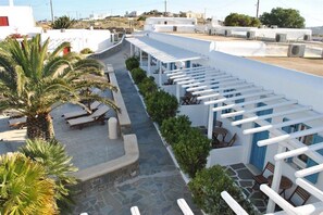 A rooftop terrace with lounge chairs and tables, surrounded by white walls and greenery.