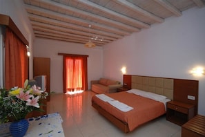 A hotel room with a wooden ceiling, a bed with a beige headboard, a nightstand, a sofa, and a TV.