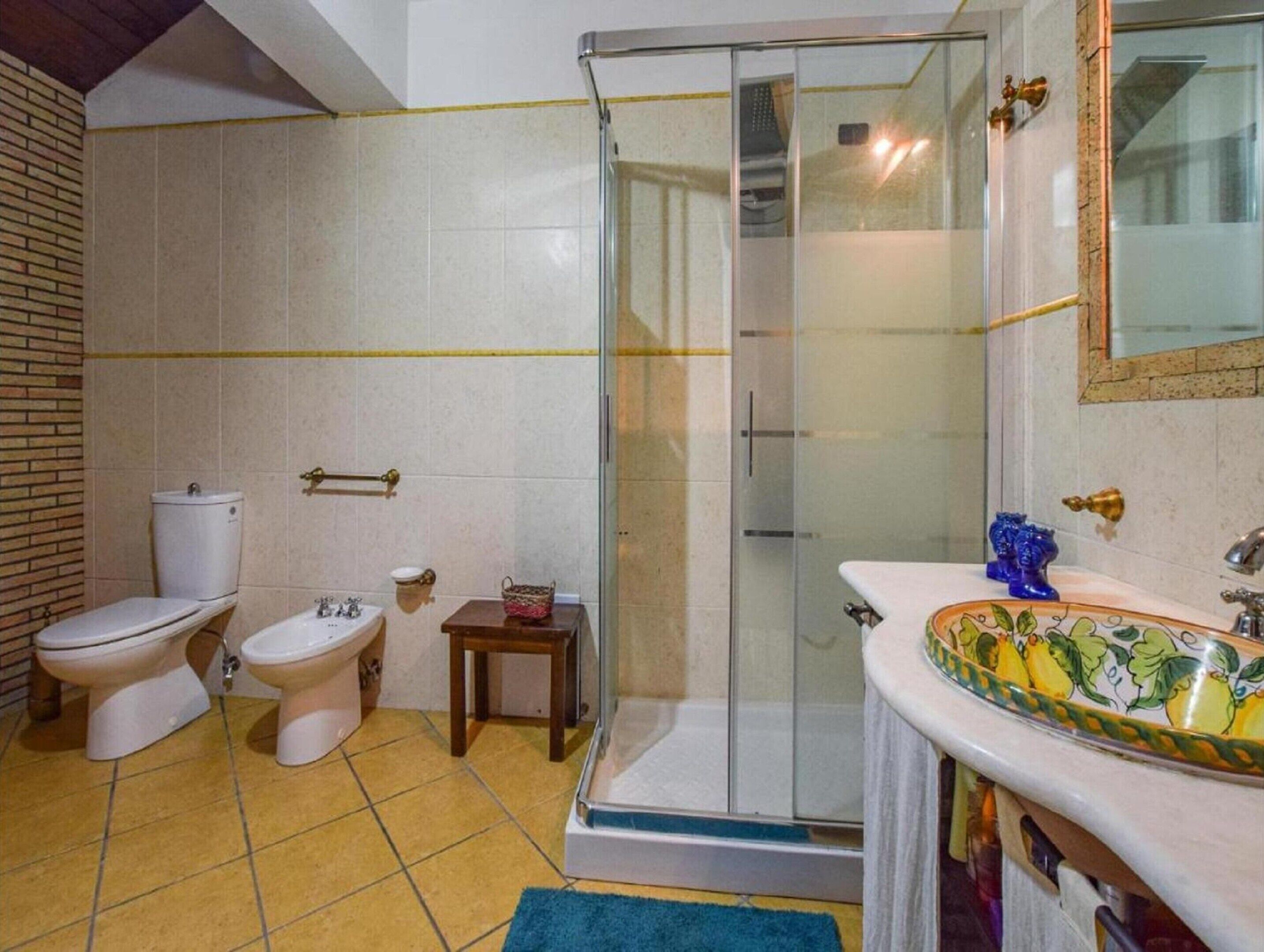 Une salle de bain avec une douche, deux toilettes, une petite table et un lavabo décoratif.