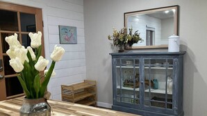 Ein Zimmer mit Holzboden, einer Vase mit weißen Blumen, einem Schrank mit Glastüren und einem Spiegel an der Wand.