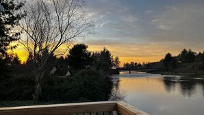 Eine Holzterrasse mit Blick auf einen stillen See, Bäume und einen Sonnenuntergang im Hintergrund.