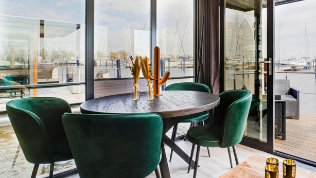 Ein moderner Essbereich mit rundem Tisch und grünen Stühlen, mit Blick auf einen Yachthafen und Boote.