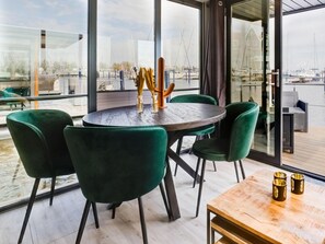 Un espace repas moderne avec une table ronde et des chaises vertes, donnant sur une marina où sont amarrés des bateaux.
