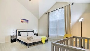 Un dormitorio con cama, mesitas de noche, ventilador de techo, ventana con cortinas y vistas al exterior.