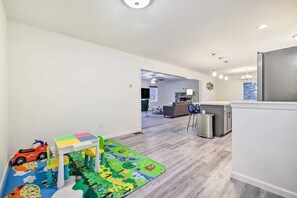 A spacious living area with a kitchen in the background, a play area with toys, and a large window providing natural light.