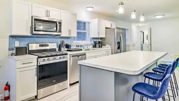 Una cocina moderna con electrodomésticos de acero inoxidable, armarios blancos y una isla grande con taburetes de bar.