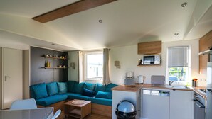 A compact living space with a sofa, a small dining table, a kitchen area with a microwave and stove, and a trash bin. - Chalet in Oostkapelle Near Beach & Pool (Oostkapelle)