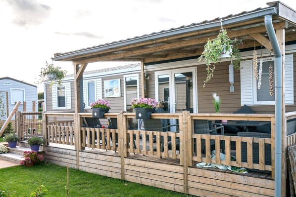 A wooden deck with outdoor furniture, potted plants, and a view of neighboring houses.