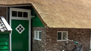 A green building with a thatched roof, a bicycle, and a brick wall. - Farmhouse in Staphorst With Sauna (Rouveen)