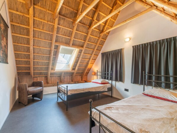 A bedroom with a sloped ceiling, a single bed, a chair, and a window.