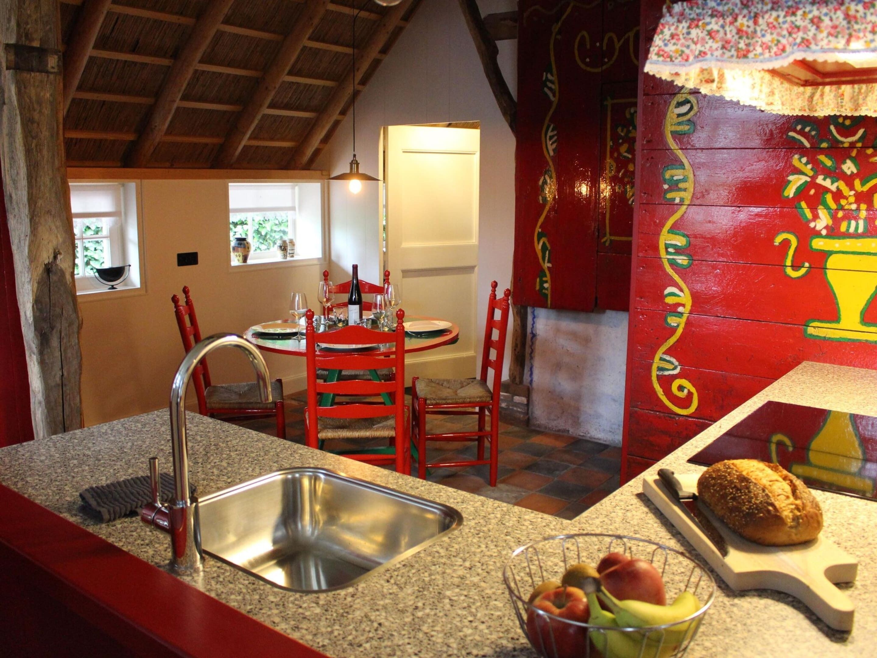 Una cocina con encimeras de granito, un fregadero de acero inoxidable, sillas rojas y una mesa de comedor con sillas.