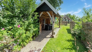 A rustic wooden structure with a pitched roof, a brick pathway leading to it, and a well-maintained garden with various plants and flowers. - Farmhouse in Staphorst With Sauna (Rouveen)