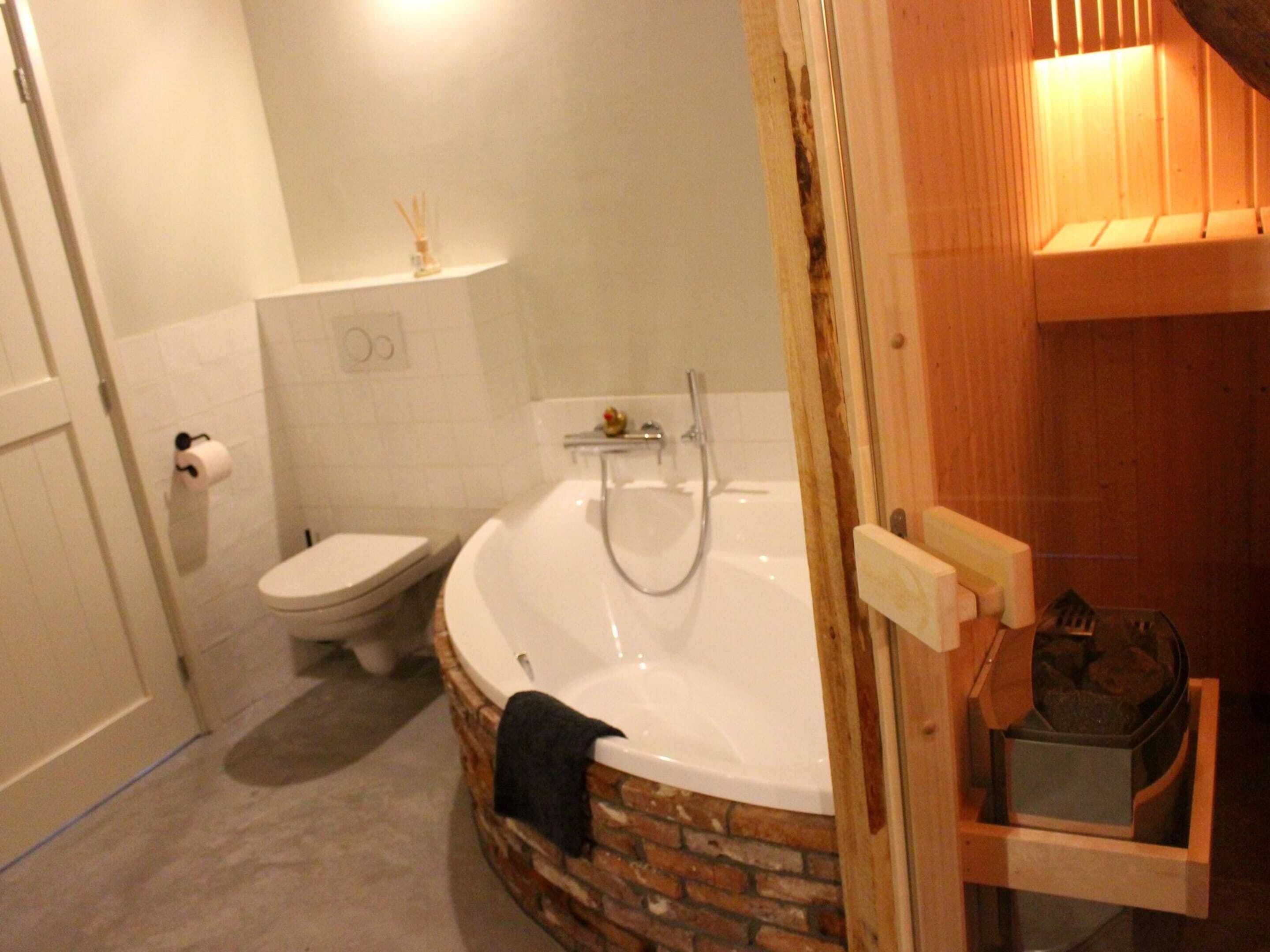 A bathroom with a white toilet, a white bathtub, and a wooden shelf with a trash bin.