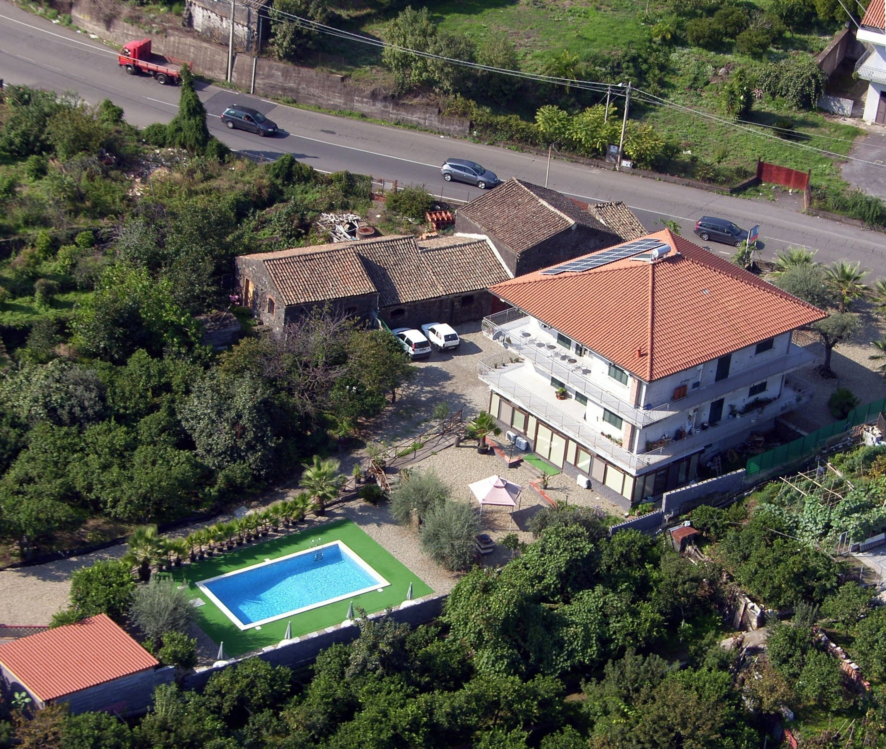 A multi-story building with a red-tiled roof, a swimming pool, and a parking area.