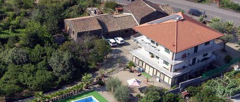 A multi-story building with a red-tiled roof, a swimming pool, and a parking area.