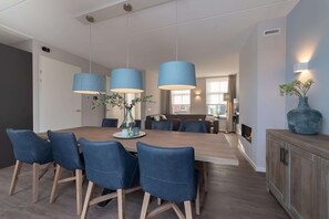 A modern dining area with a wooden table, blue upholstered chairs, and pendant lights. - Holiday Home Colijnsplaat Near Beaches (Colijnsplaat)