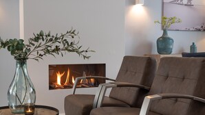 Uma sala de estar moderna com lareira, poltronas de couro, um vaso de vidro com folhagem e um vaso azul sobre uma mesa lateral de madeira.