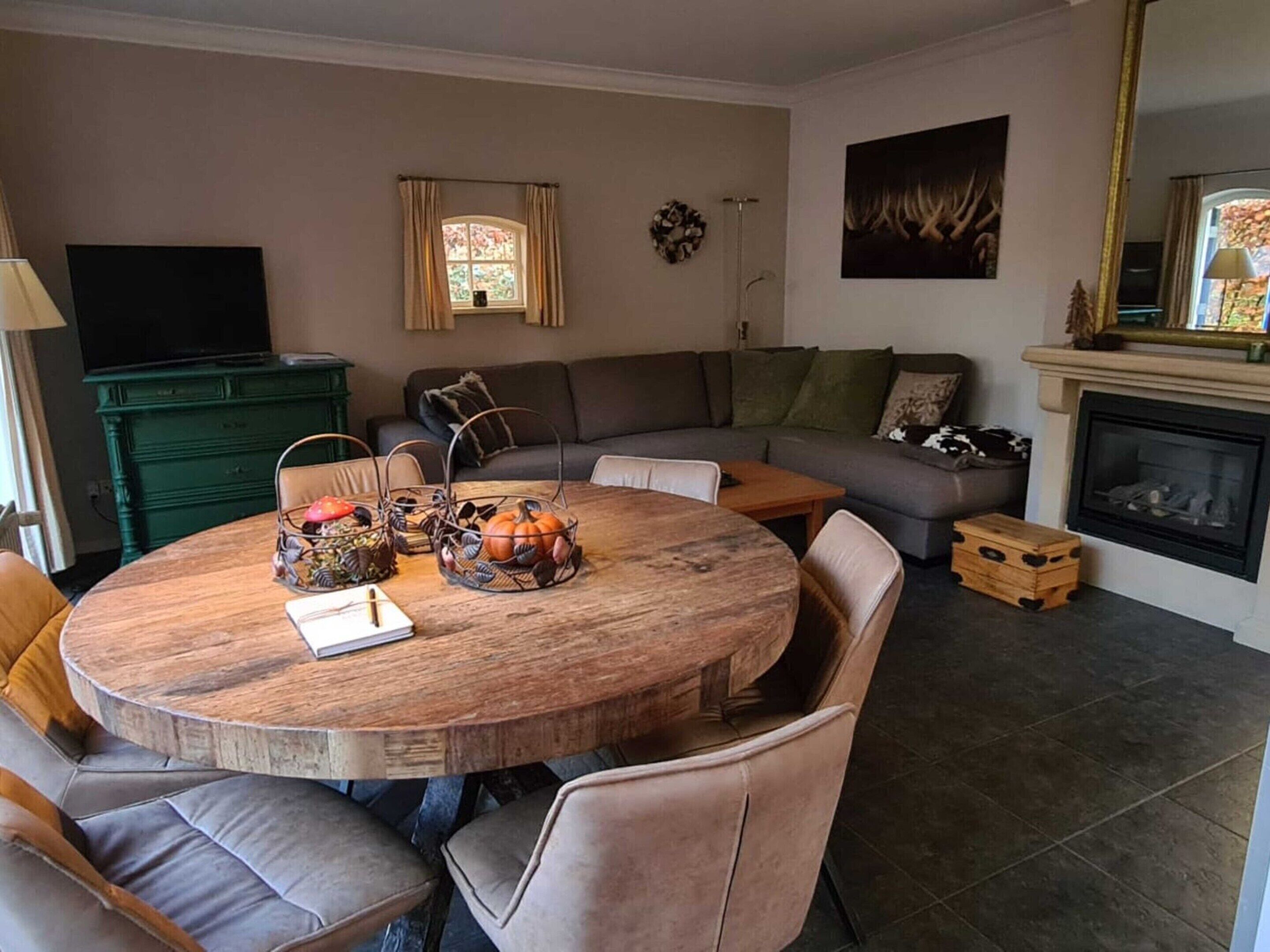 Una sala de estar con una mesa redonda de madera, sillas con cojines, un sofá, una chimenea y un televisor.