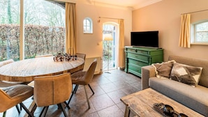 Un salón acogedor con una mesa de comedor redonda de madera, asientos cómodos, un aparador verde, un televisor de pantalla plana y un sofá con cojines.