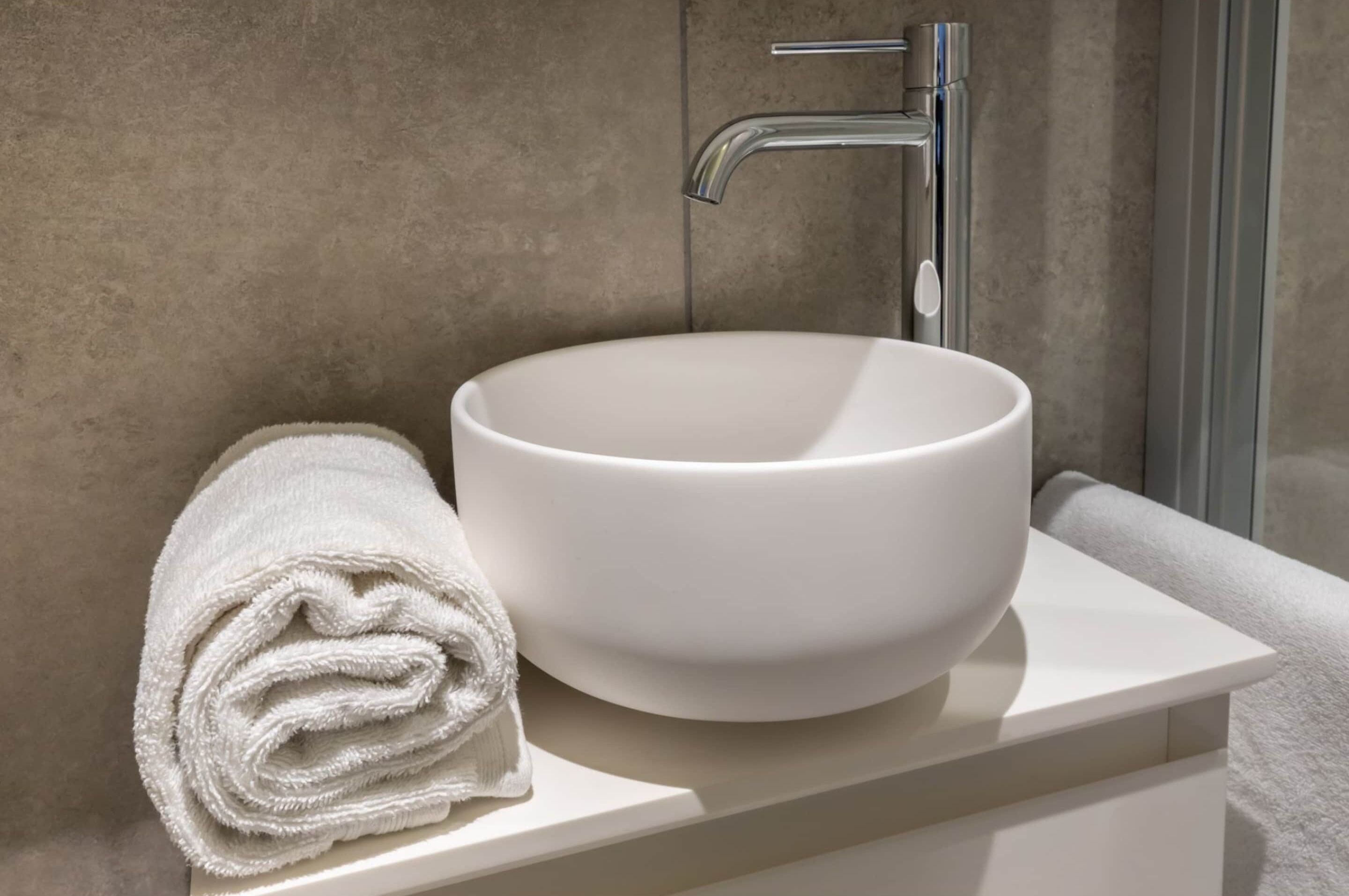 A bathroom with a white sink, a towel, and a modern faucet.