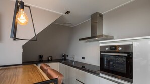 A modern kitchen with a built-in oven, stainless steel range hood, and a wooden dining table with a bench. - Apartment Right in the Centre of Domburg (Domburg)