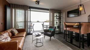 A modern living room with a leather sofa, a round coffee table, a black armchair, and a dining area with bar stools. - Apartment Right in the Centre of Domburg (Domburg)