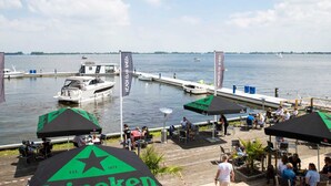 A waterfront restaurant with outdoor seating, a dock with boats, and a view of the water. - Houseboat Sneekermeer With Garden and Views (Offingawier)