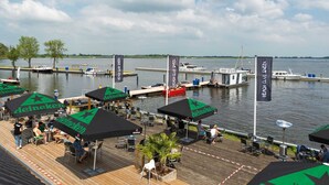 A waterfront restaurant with outdoor seating, Heineken branded umbrellas, and a view of the water. - Houseboat Sneekermeer With Garden and Views (Offingawier)