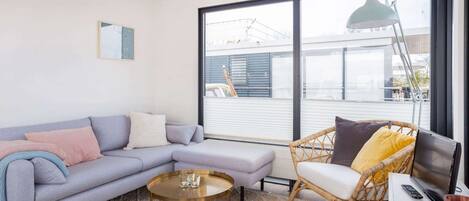 A modern living room with a sofa, a chair, a coffee table, a TV, and a large window with a view of the outside.