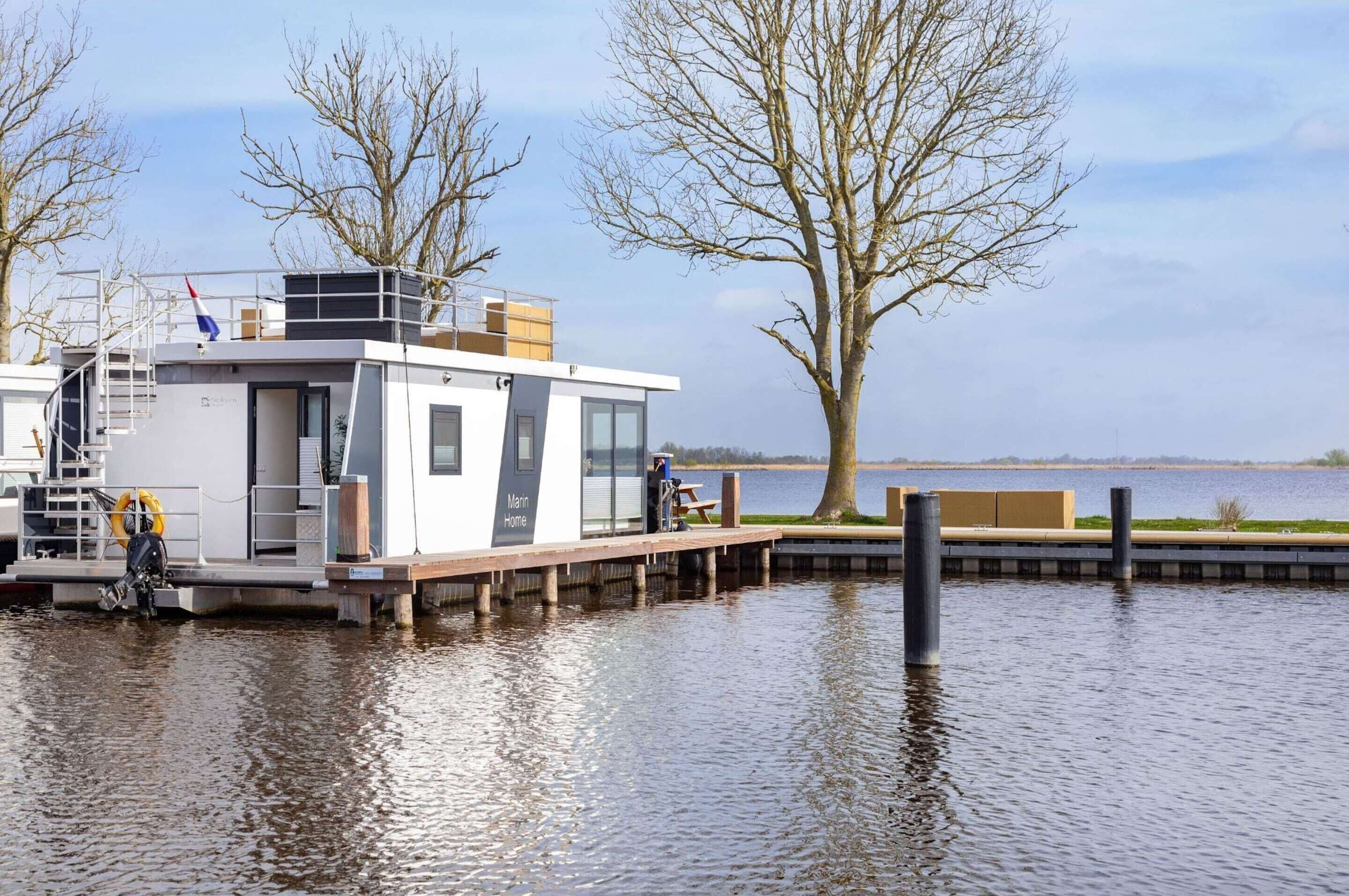 Una moderna casa flotante con un muelle, una escalera y un flotador.