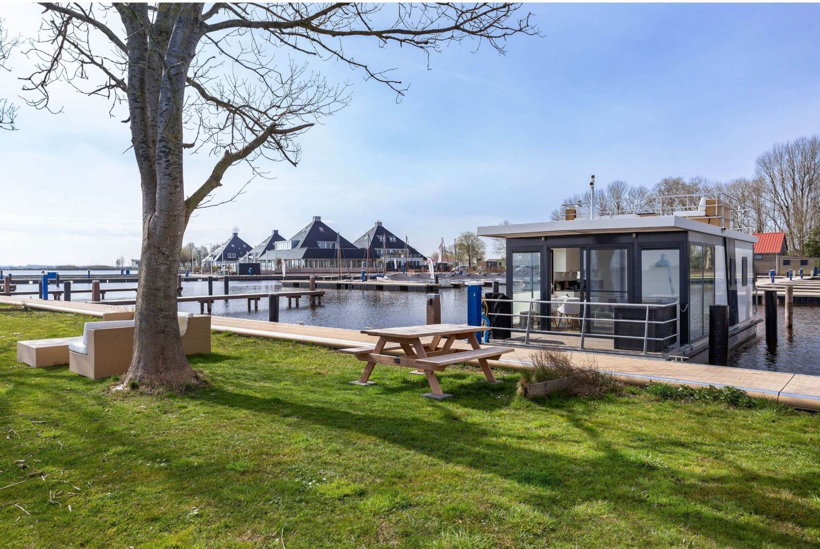 A riverside area with a dock, a wooden bench, and a modern building with large windows.