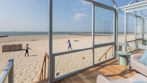 A beach view from a room with large windows, a wooden deck, and a white sofa. - House in Dishoek With Sea Views (Koudekerke)
