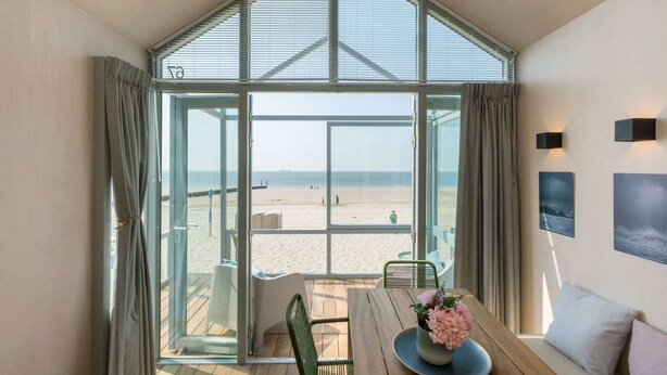 A room with a large glass door leading to a beach view, a wooden table with chairs, and a sofa. - House in Dishoek With Sea Views (Koudekerke)