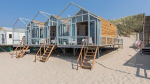 A beach house with a wooden deck, glass walls, and a sandy beach setting. - House in Dishoek With Sea Views (Koudekerke)