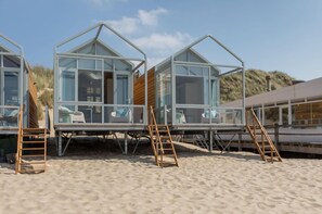 Beach huts with glass walls, wooden floors, and wooden railings. - House in Dishoek With Sea Views (Koudekerke)