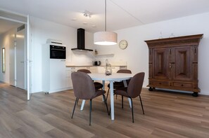 A modern kitchen with a white dining table, brown chairs, a wooden cabinet, and a clock on the wall. - Breathtaking Penthouse Views (Kamperland)