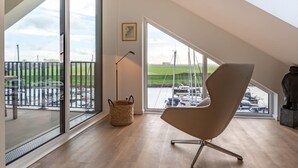 Ein geräumiges Zimmer mit großen Fenstern, die auf eine Marina blicken, ein moderner Sessel und ein kleiner Tisch.