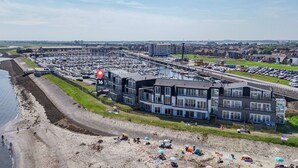 Un port de plaisance avec des bateaux, une plage où se trouvent des gens, et des bâtiments modernes.