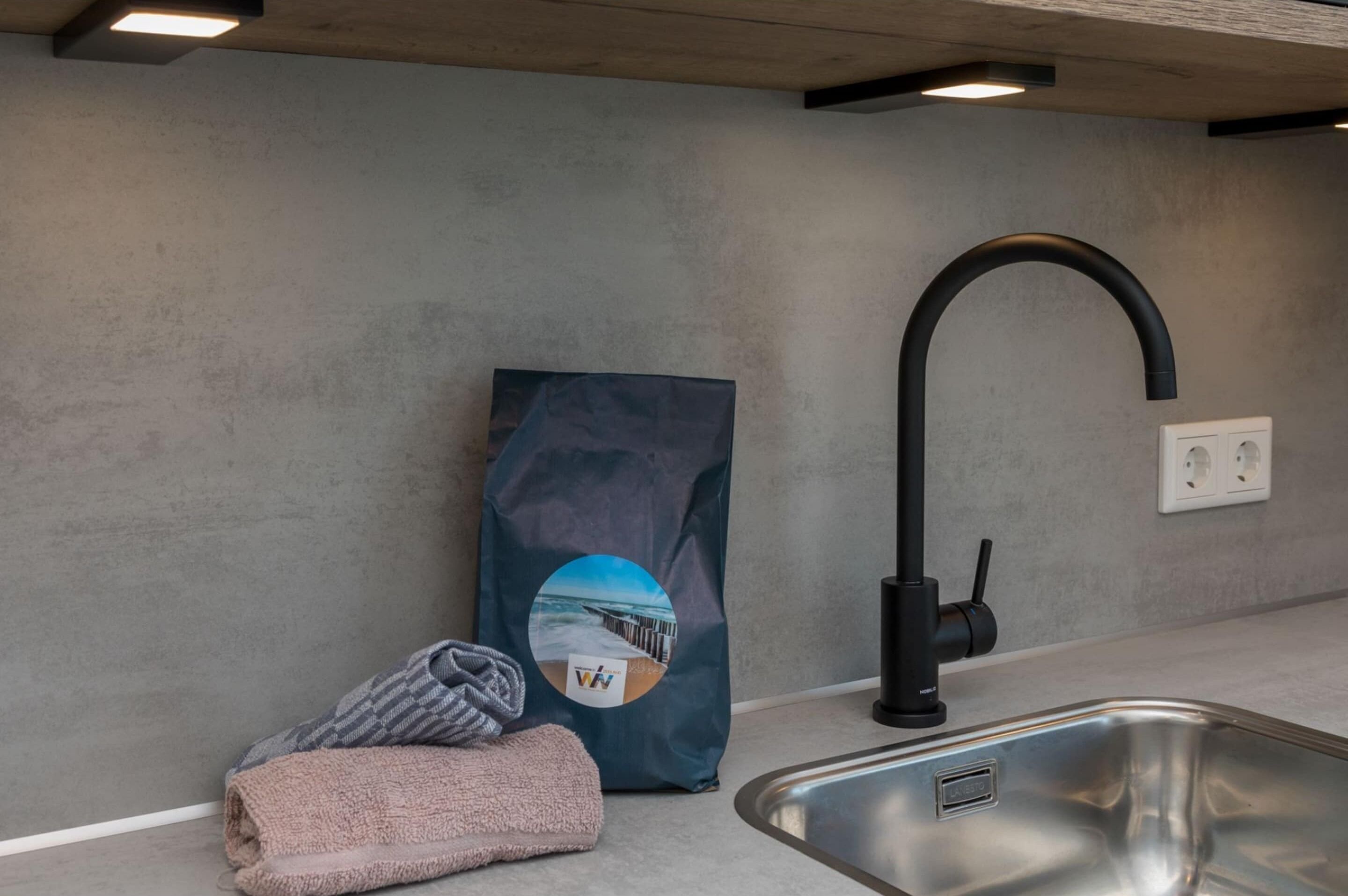 Eine moderne Küche mit Spüle aus Edelstahl, einem schwarzen Wasserhahn und einem Handtuch auf der Arbeitsplatte.