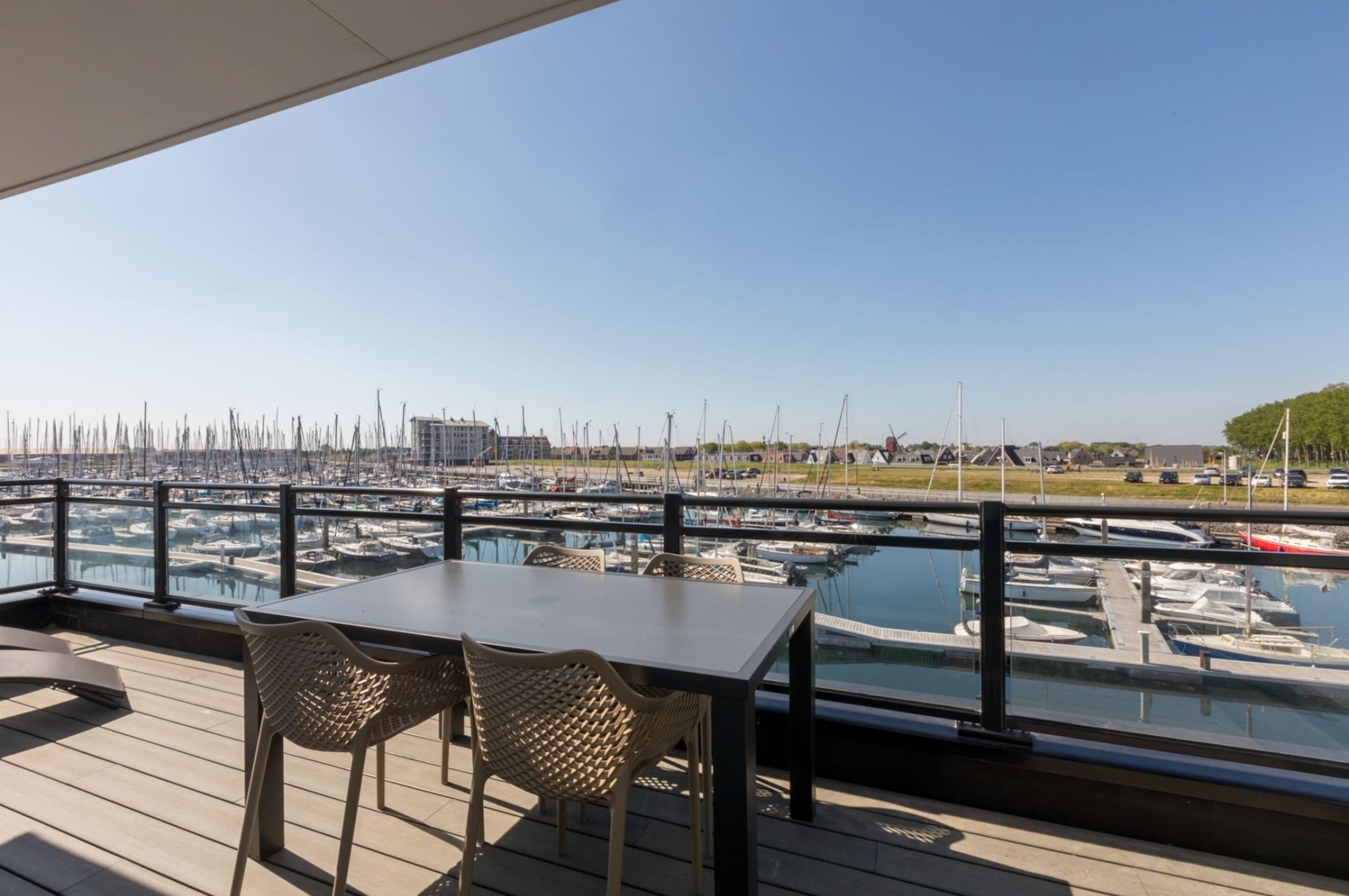 Terraza con mesa y sillas con vista a un puerto deportivo lleno de barcos.