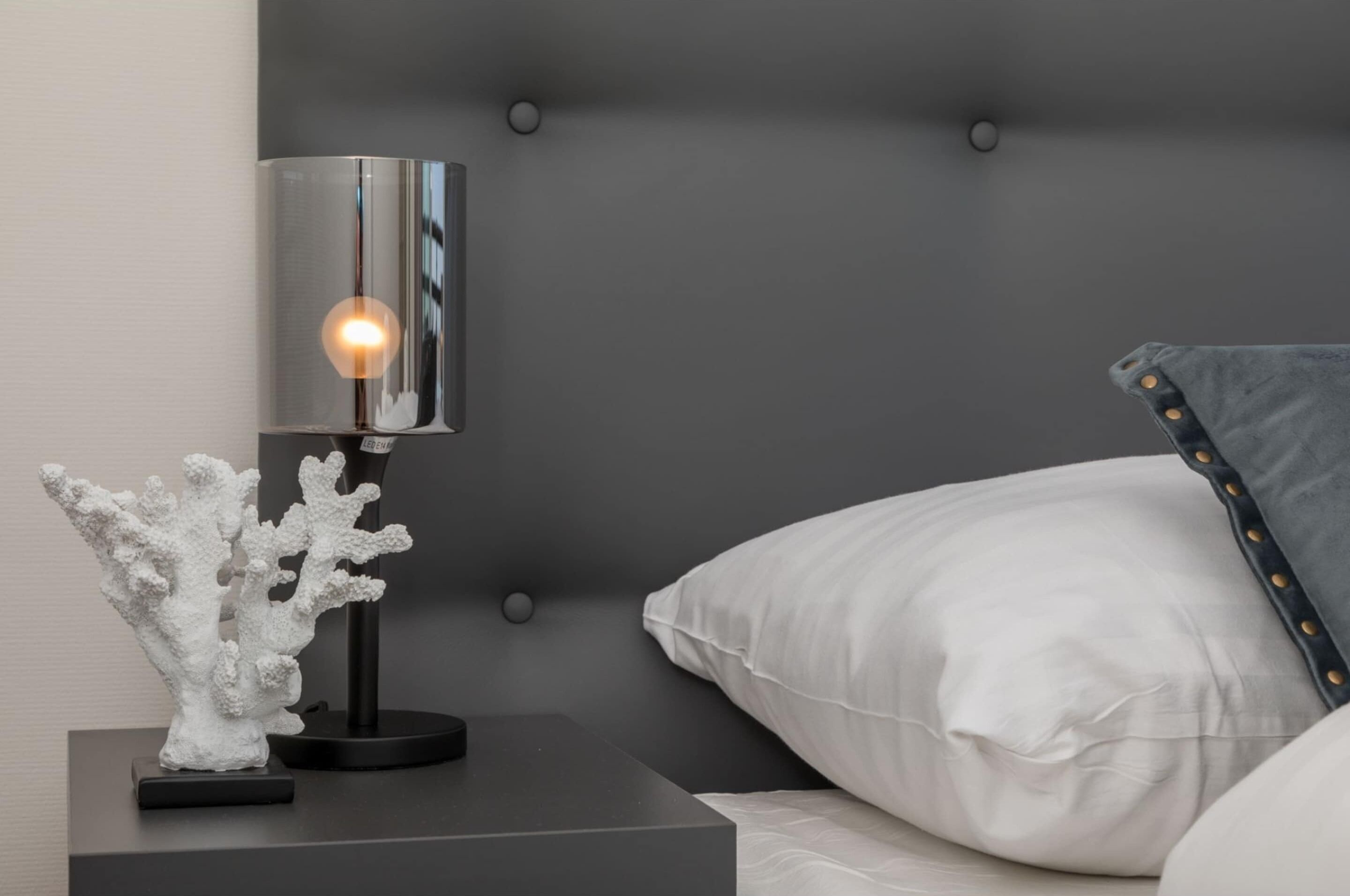 A modern bedroom with a tufted headboard, a bedside table with a lamp, and a decorative coral sculpture.
