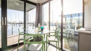 A modern room with a view of a marina, featuring a round table with chairs, a small plant, and a bottle. - Beautiful Houseboat With Shared Pool (Volendam)