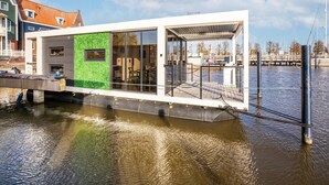 A modern houseboat with a glass facade, a green wall, and a docked in a calm water body. - Beautiful Houseboat With Shared Pool (Volendam)