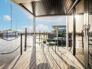 A modern outdoor deck with a glass enclosure, a green chair, and a small table with a plant. - Beautiful Houseboat With Shared Pool (Volendam)