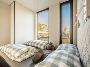 A hotel room with two beds, checkered bedding, a large window with a view of buildings, and a patterned wall. - Beautiful Houseboat With Shared Pool (Volendam)