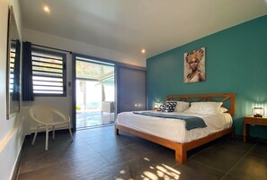 A bedroom with a bed, a chair, a painting, and a view through a sliding door.
